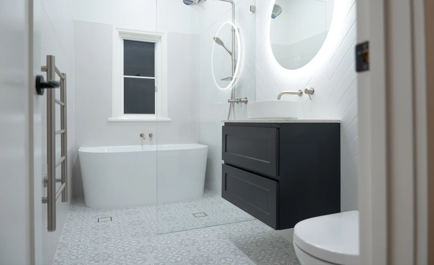 Bathroom with freestanding bath, black wall hung vanity and round backlit mirror