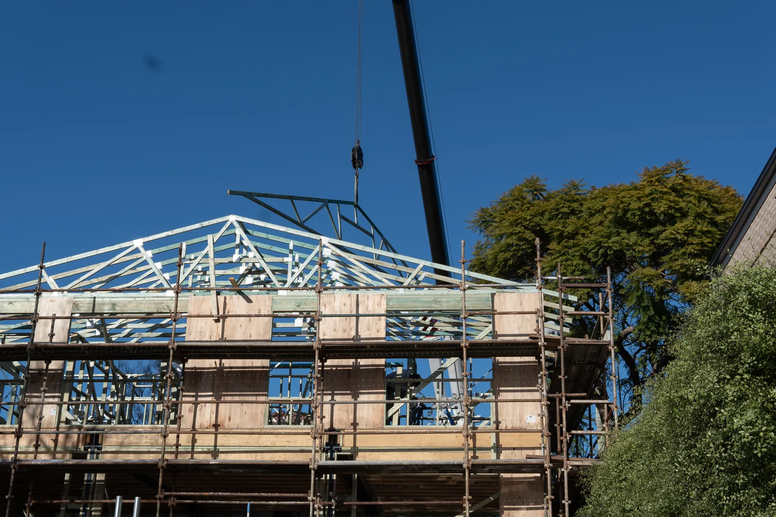 Roof trusses being lifted by crane onto the framed two storey home rebuild at Gymea, with scaffolding around the perimeter