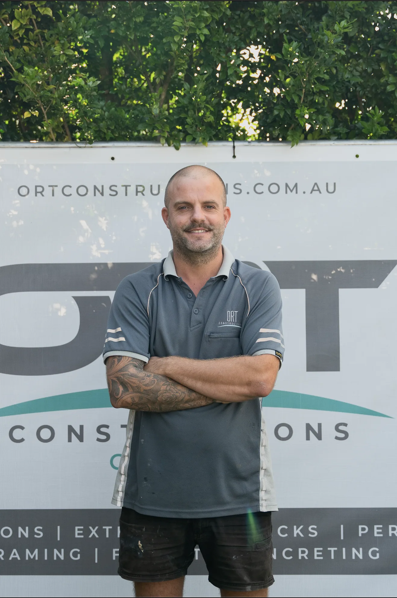 Oscar Taylor, Managing Director of ORT Constructions, standing in front of an ORT Constructions site banner